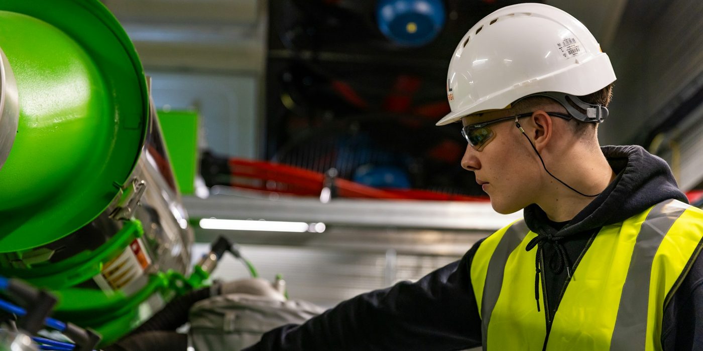 A technician in a hard hat and high-visibility vest working on plant equipment