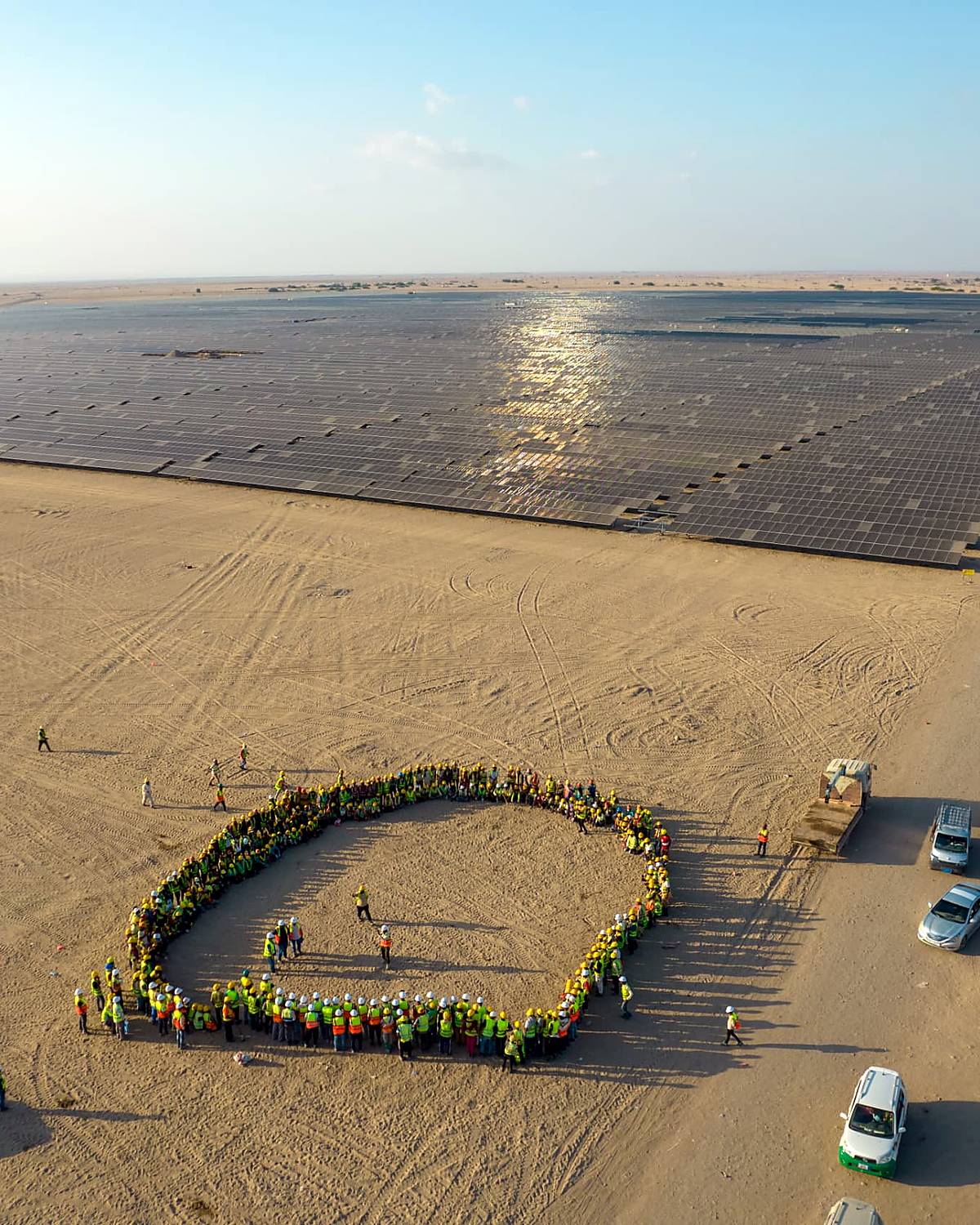A site crew of several hundred gathered in a circle at a completed solar plant